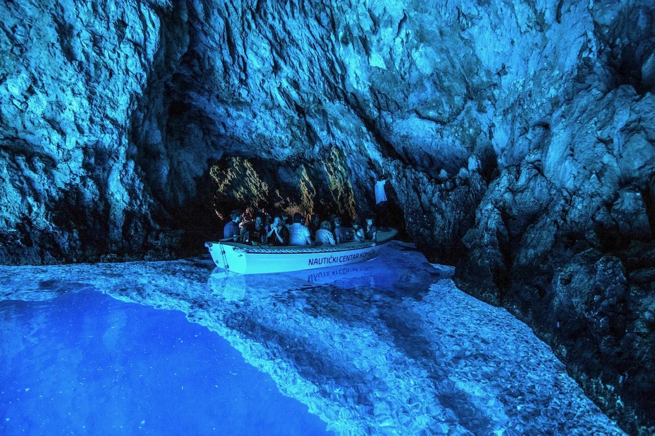 A boat of visitors inside the Blue Cave on Biševo, the water below it glowing blue. Blue Cave Group Tour
