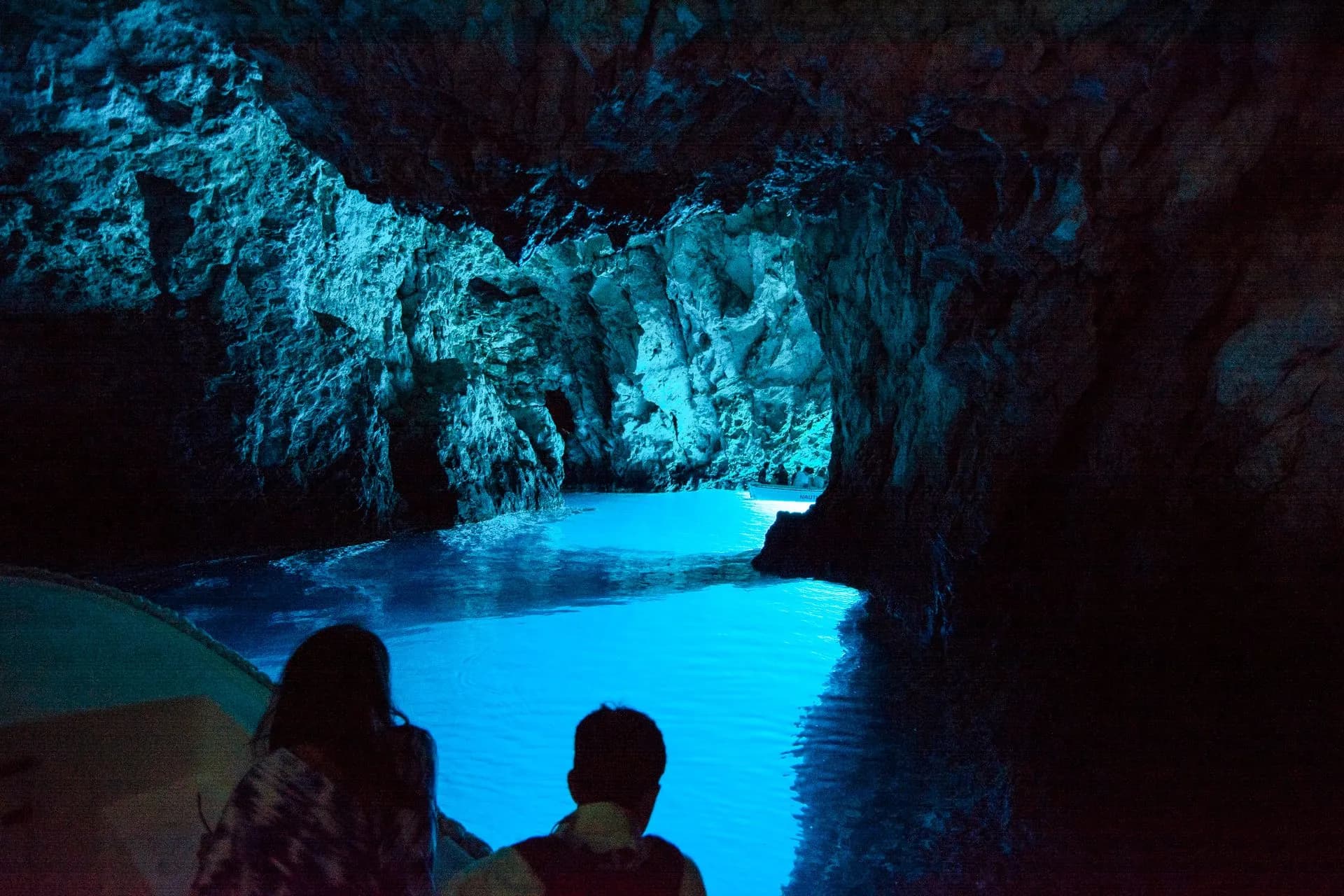 Inside the Blue Cave on Biševo from the boat, guests in silhouette against water lit that electric blue from the opening below the surface. Private Blue Cave Tour